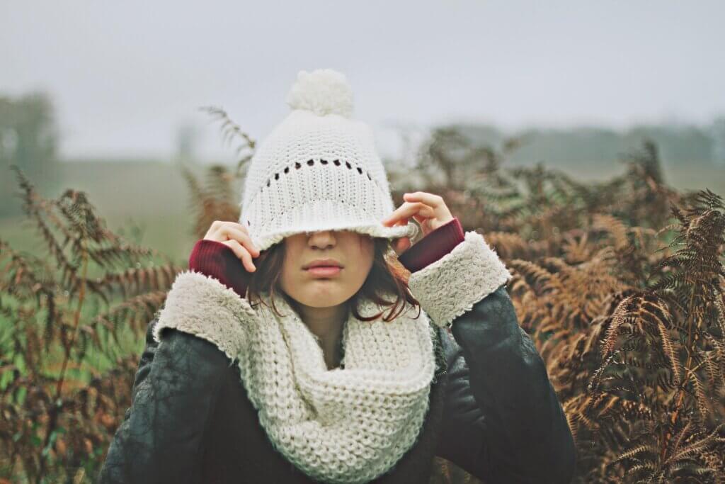 A young woman pulling her hat down over her eyes on a grey foggy day