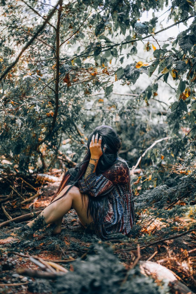 A woman sitting in a wodded area with her head in her hand hiding her face